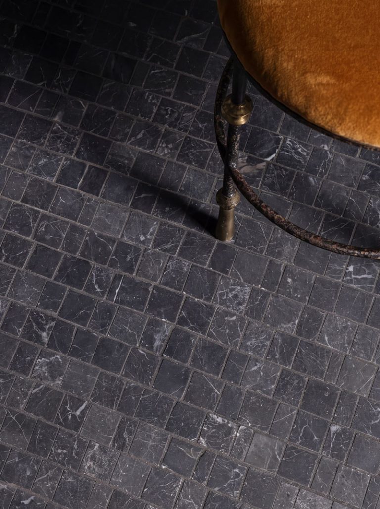 Close-up of Nero Marquina Marble Tumbled Metro Mosaic backsplash behind a white marble basin with antique brass fixtures by Starel Stones.